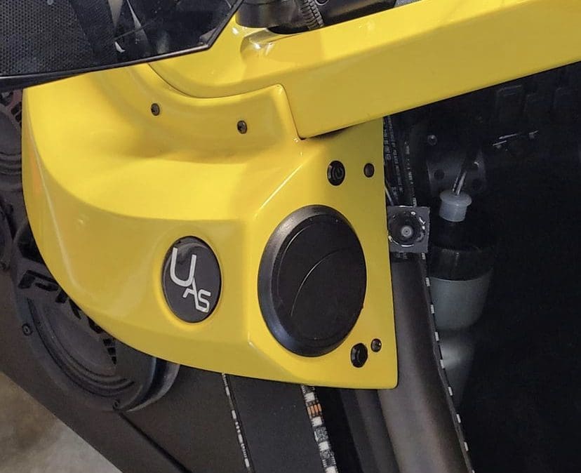 Close-up of a yellow machine part with a circular black component and small logo.