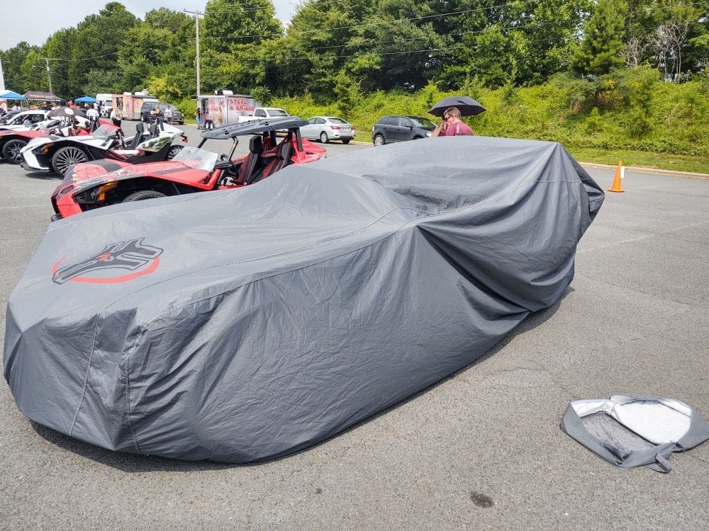 A car covered with a gray protective cover in a parking lot.