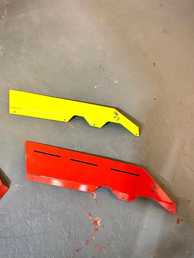 Two plastic car bumper covers, one yellow and one red, lying on the ground.