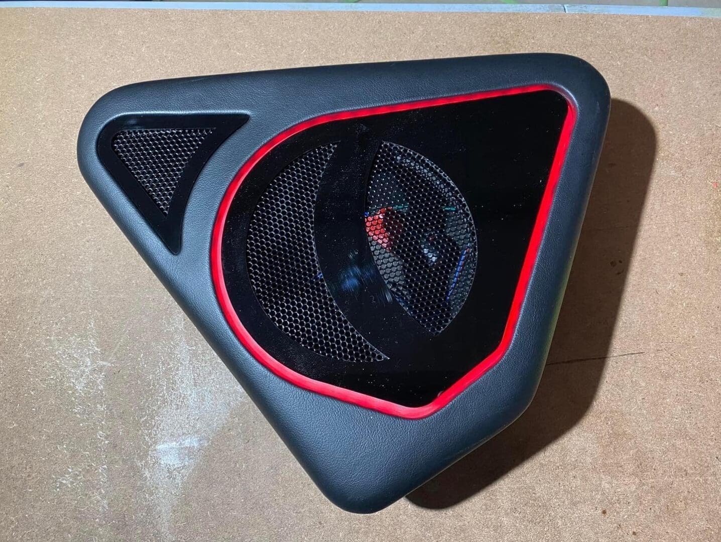 E55DF78B-0C96-4551-9FC7-E62B7F2EF295 (1) Triangular speaker grill with red accent on a brown surface.