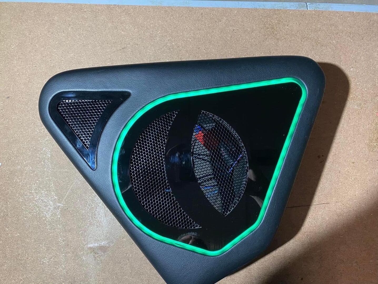 F13A5AEB-49C0-477E-9DC7-55D9AF88EC59 Triangular speaker grill with green trim on a wooden surface.