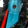 Close-up of a blue motorcycle fuel tank with a red and black emblem.