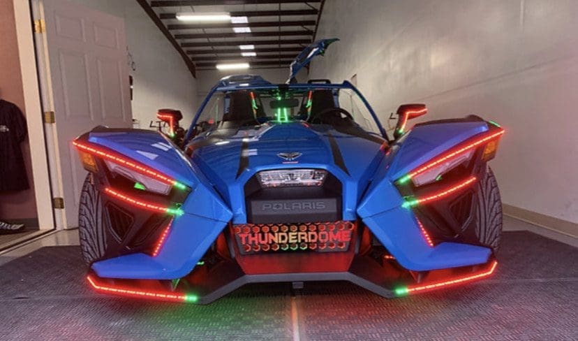 A vibrant blue futuristic three-wheeled vehicle with glowing red and green lights.