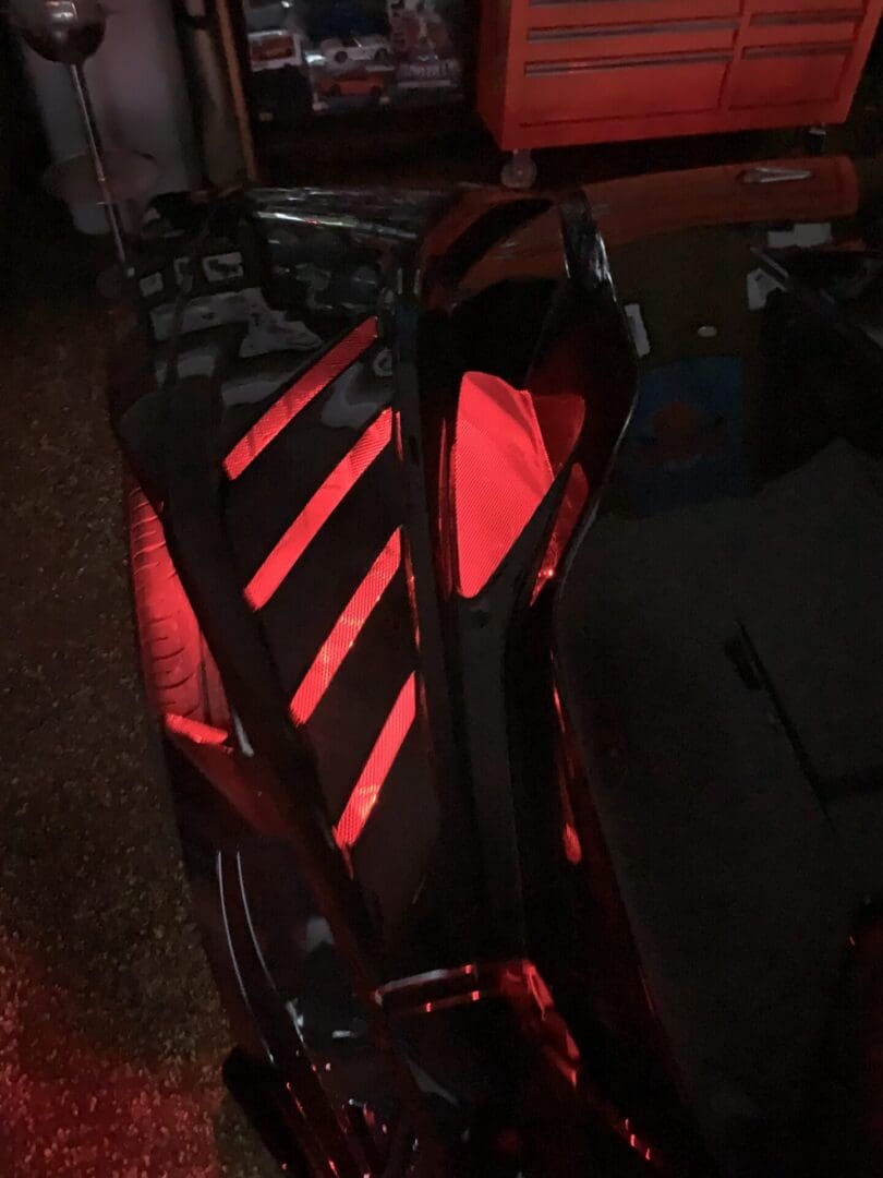 Close-up of a black car hood with red illuminated vents in a dim garage.