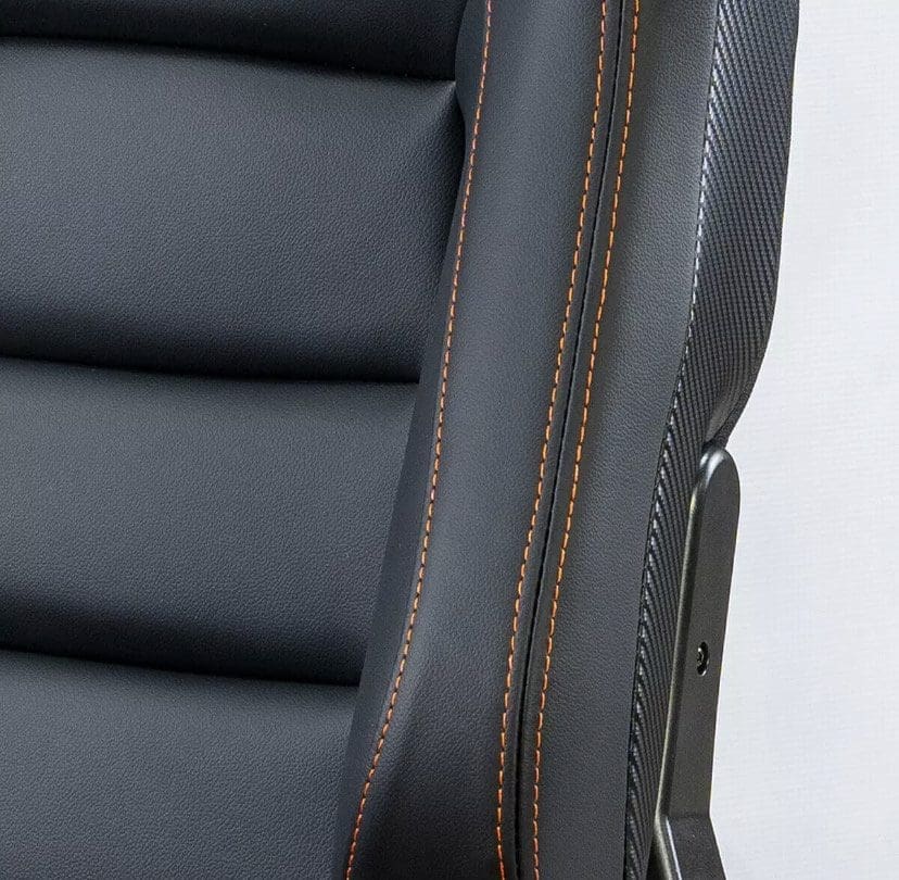 Close-up of a black leather chair with orange stitching and carbon fiber accents.