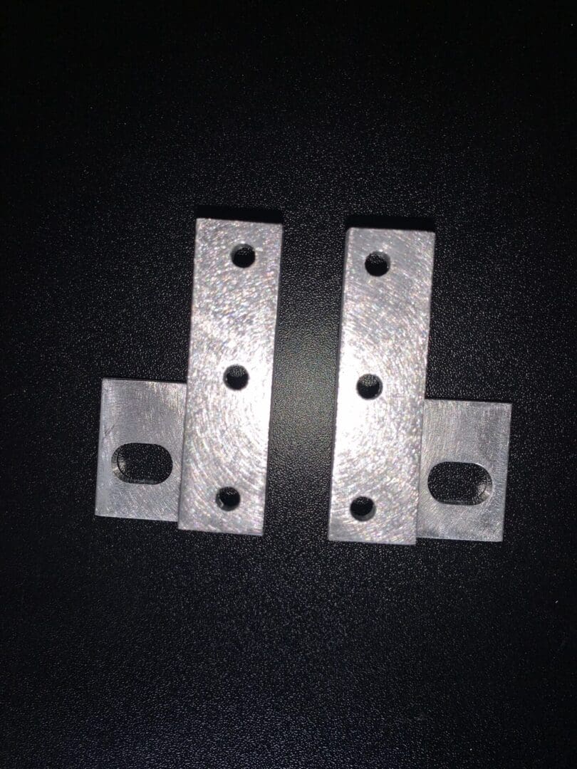 Two metal brackets with multiple holes on a black background.