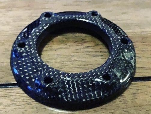 Close-up of a black textured circular object with holes, on a wooden surface.