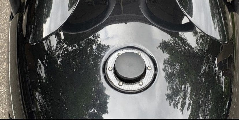 Close-up of a shiny black motorcycle fuel tank with a chrome fuel cap.