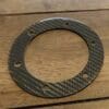 Carbon fiber circular gasket with six holes on a wooden surface.