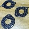 Three black carbon fiber washers with different shapes on a wooden surface.
