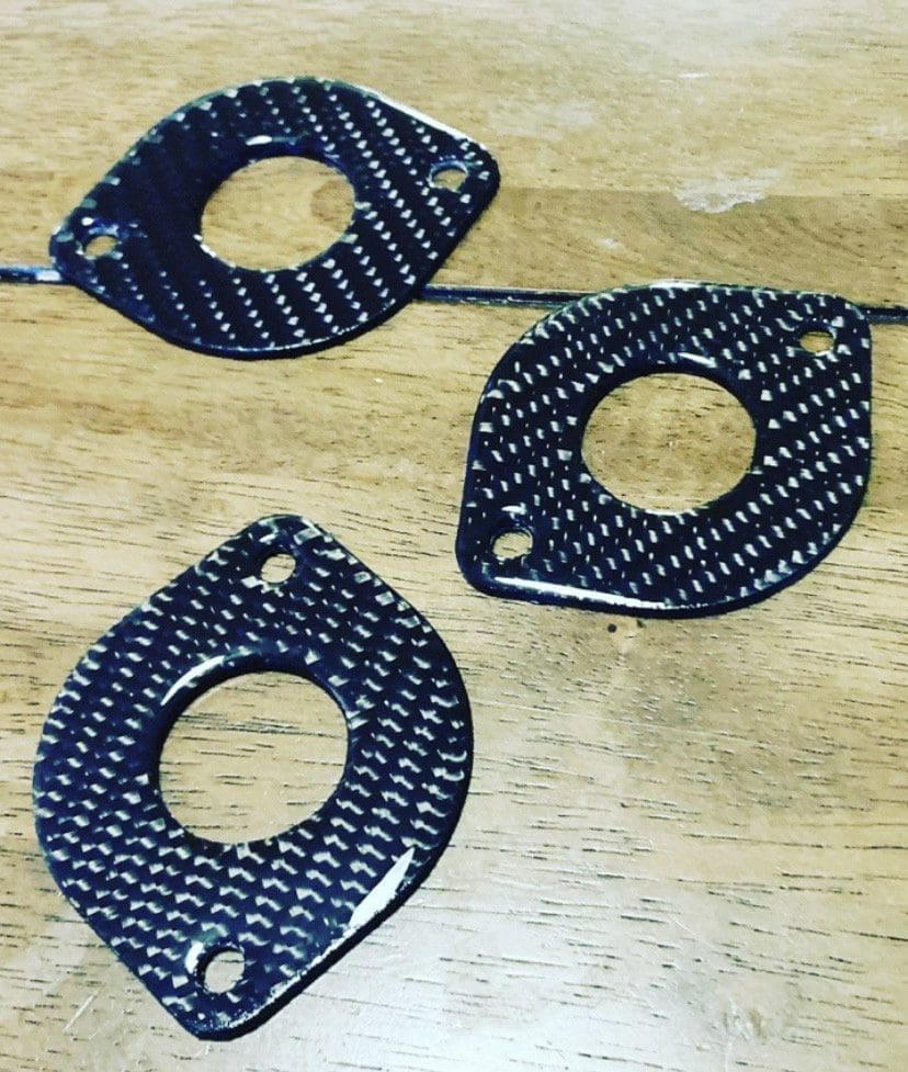 Three black carbon fiber washers with different shapes on a wooden surface.