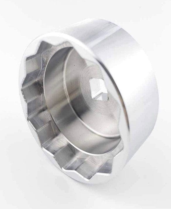 A metal tool with a ridged, circular shape and square hole in the center.
