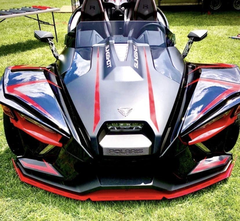 A sleek black and red Polaris Slingshot parked on grass.