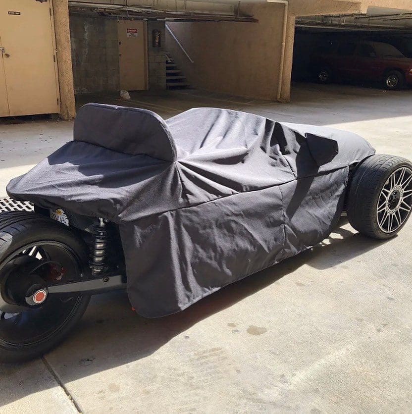 Three-wheeled vehicle covered with a black cloth in a parking garage.