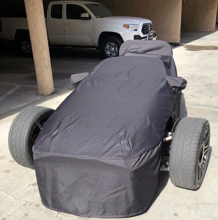 A car covered with a black protective cover in a garage.