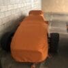 Cars covered in orange protective covers in a garage.
