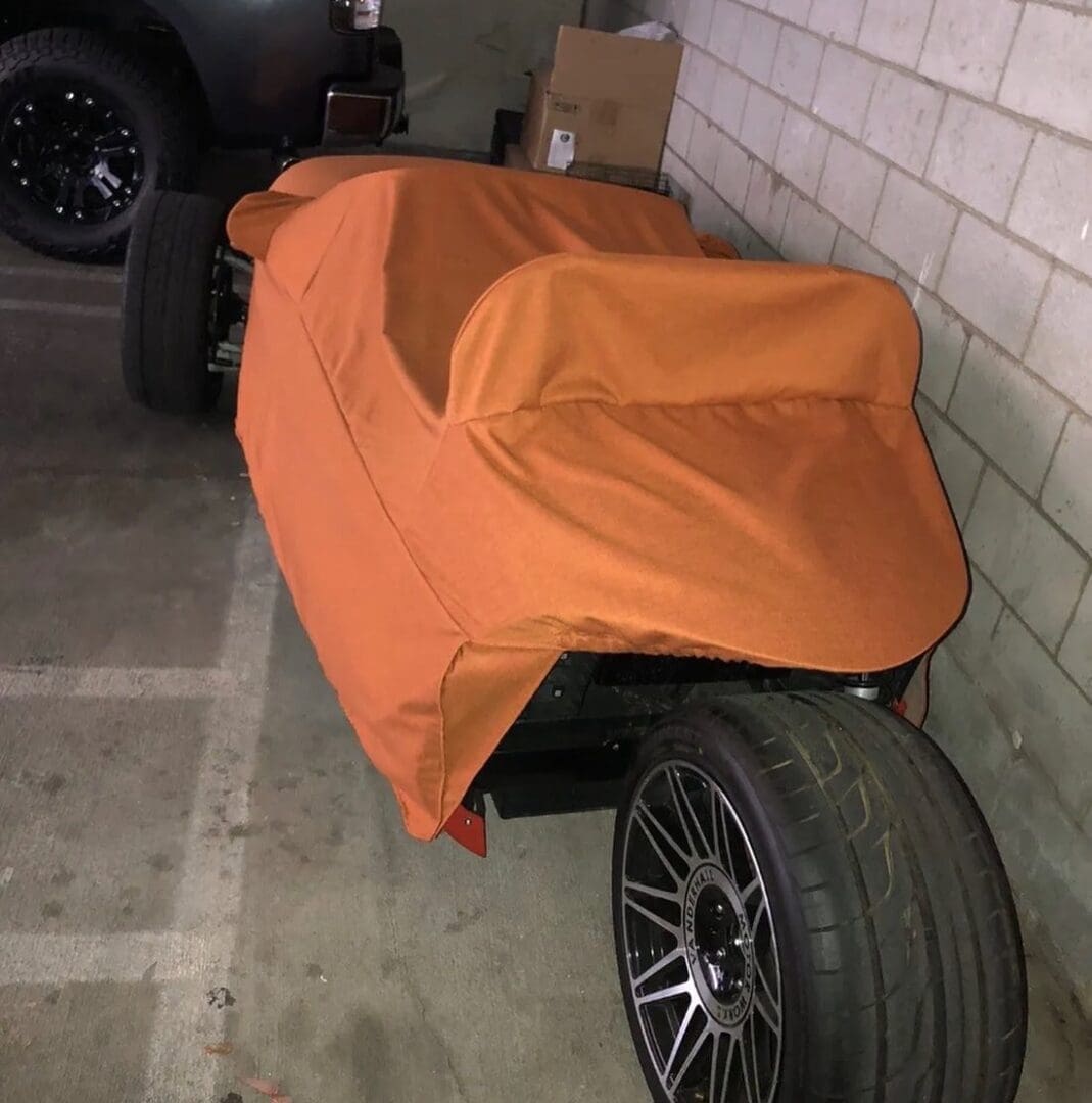 A motorcycle covered with an orange cloth in a parking area.