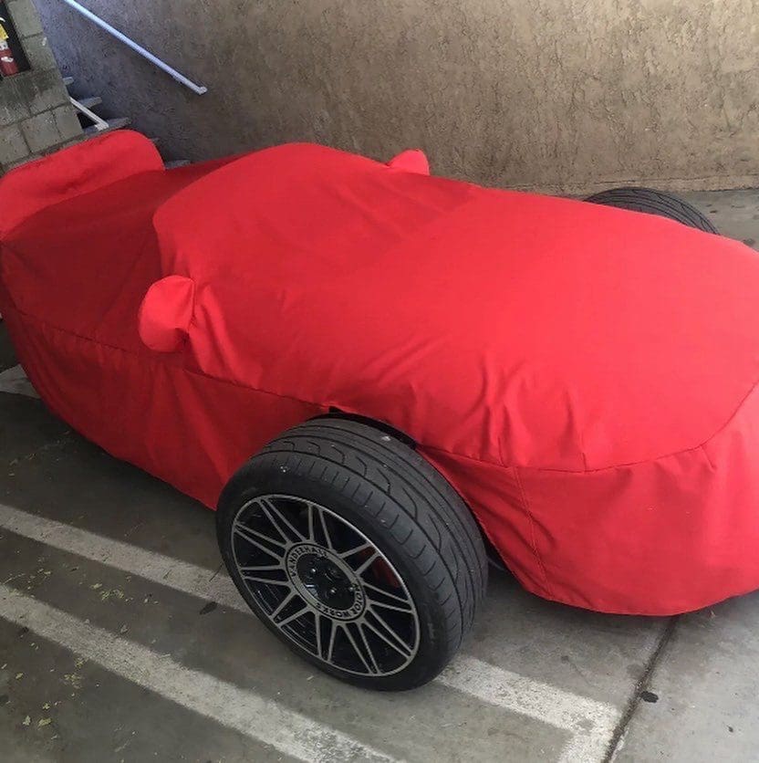 A car covered with a red protective cover, with visible black wheels.