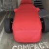 A small race car covered in a red cloth in a parking space.