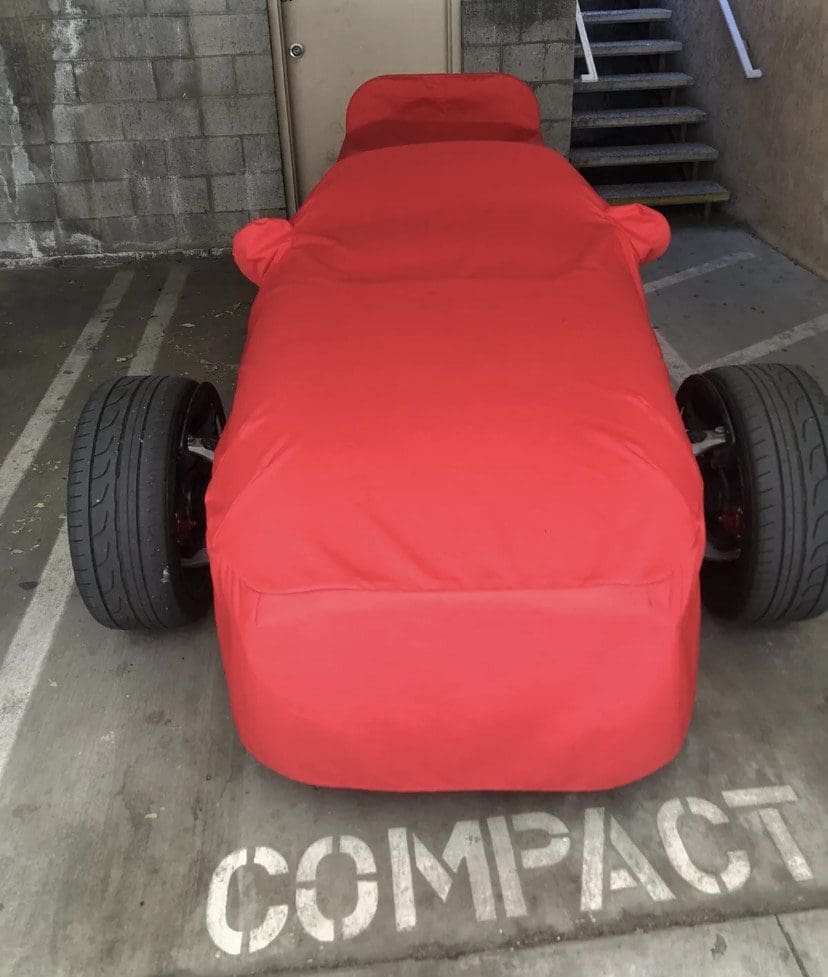 A small race car covered in a red cloth in a parking space.