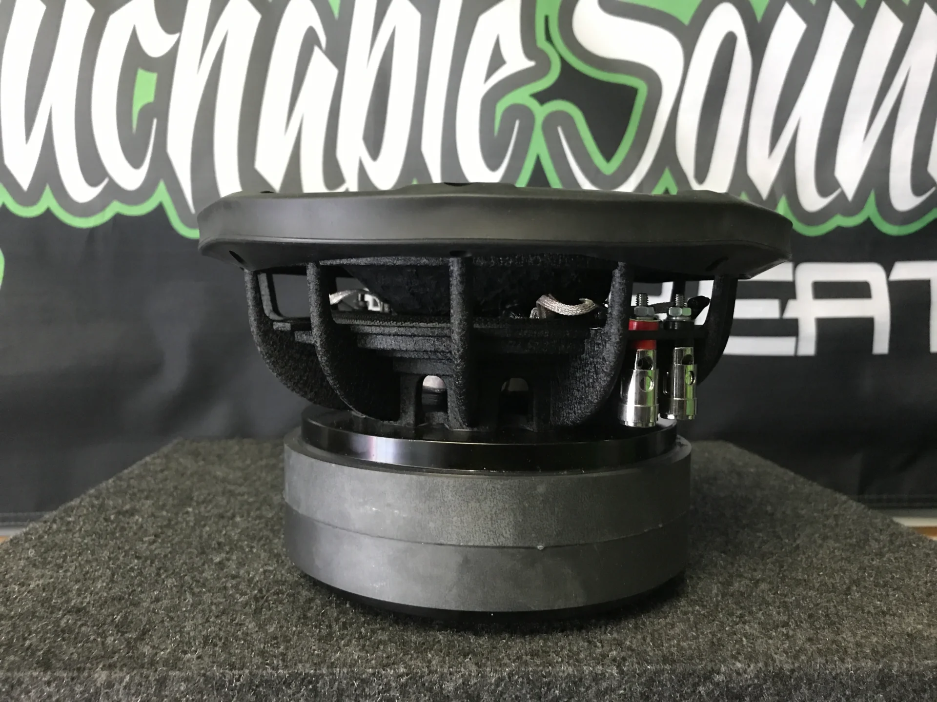 Side view of a black subwoofer speaker on a gray surface.