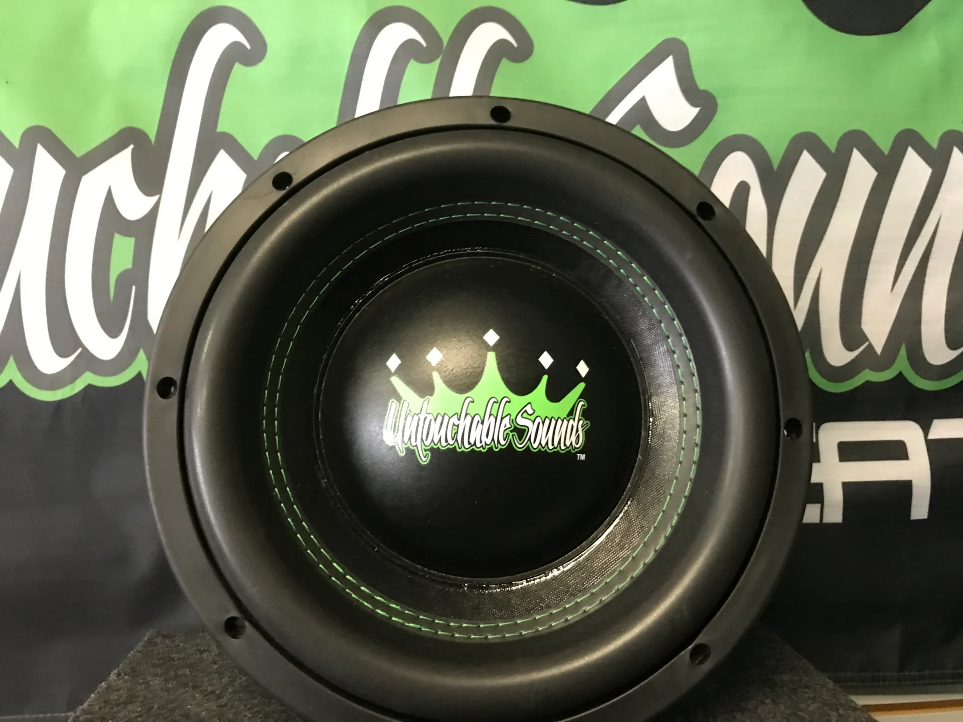 Close-up of a black subwoofer speaker with a green crown logo.