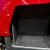 Empty carpeted compartment in a vehicle with a red exterior.