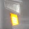 Close-up of a vehicle's orange indicator light and side mirror.