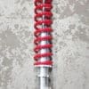 Close-up of a red coil spring suspension component on a concrete floor.