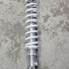 A silver coil spring shock absorber on a concrete floor.