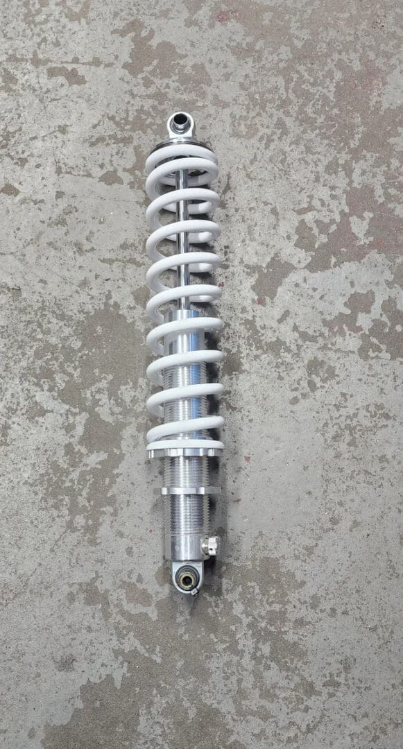 A silver coil spring shock absorber on a concrete floor.
