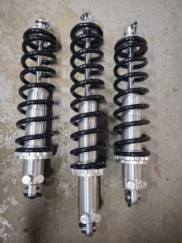 Three black coilover suspension springs with silver mounts.