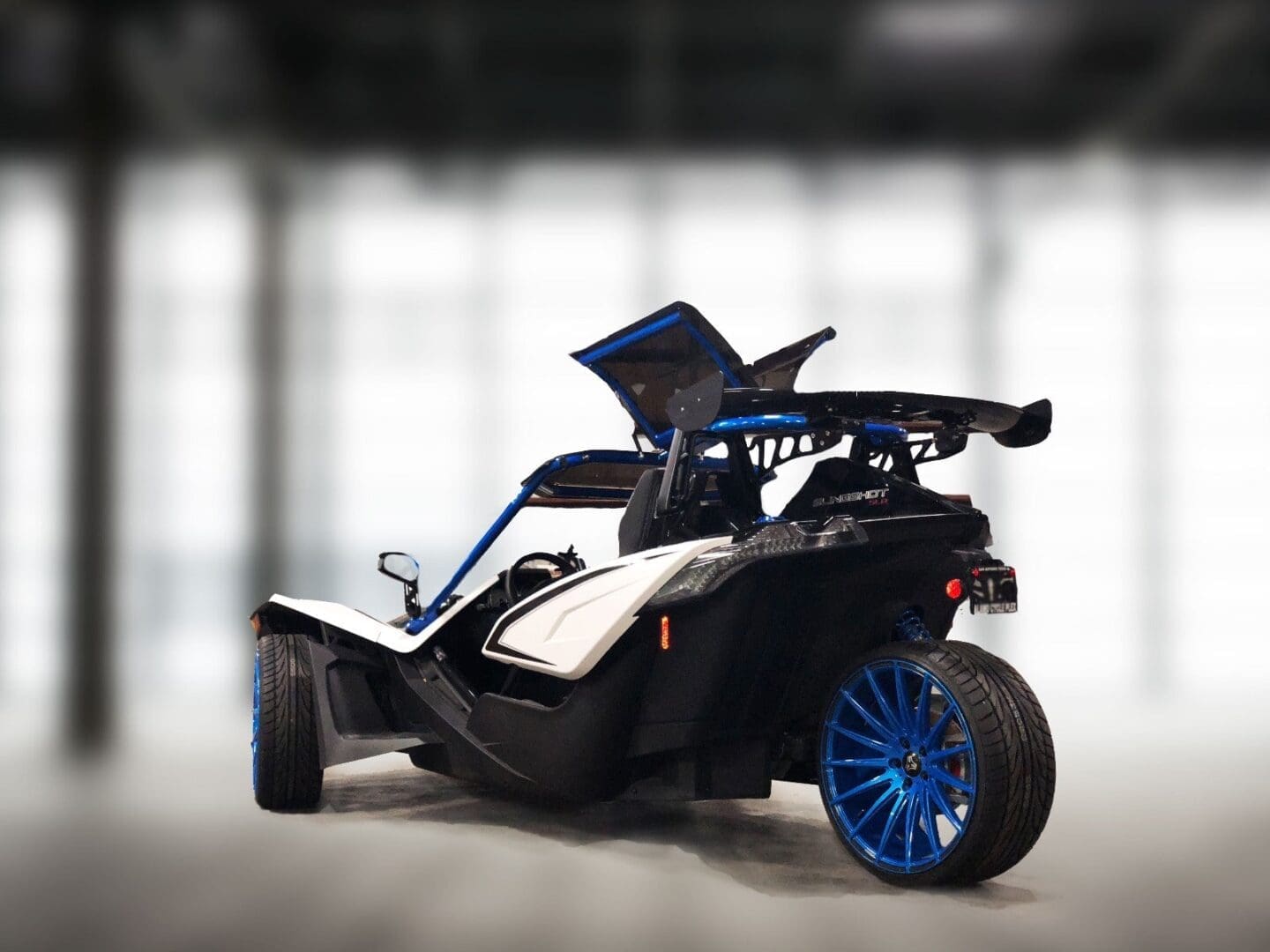 A sleek black three-wheeled car with blue rims and an open gullwing door.