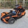 Orange and black three-wheeled sports vehicle parked outdoors.