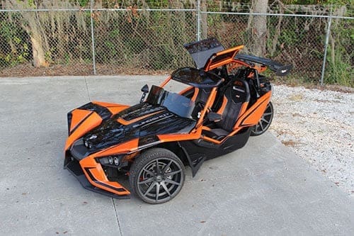 Orange and black three-wheeled sports vehicle parked outdoors.