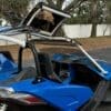 Man driving a blue dune buggy with a roll cage and open roof.