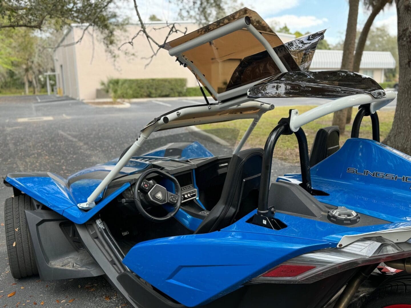 A blue sports car with its doors and hood open in a parking lot.